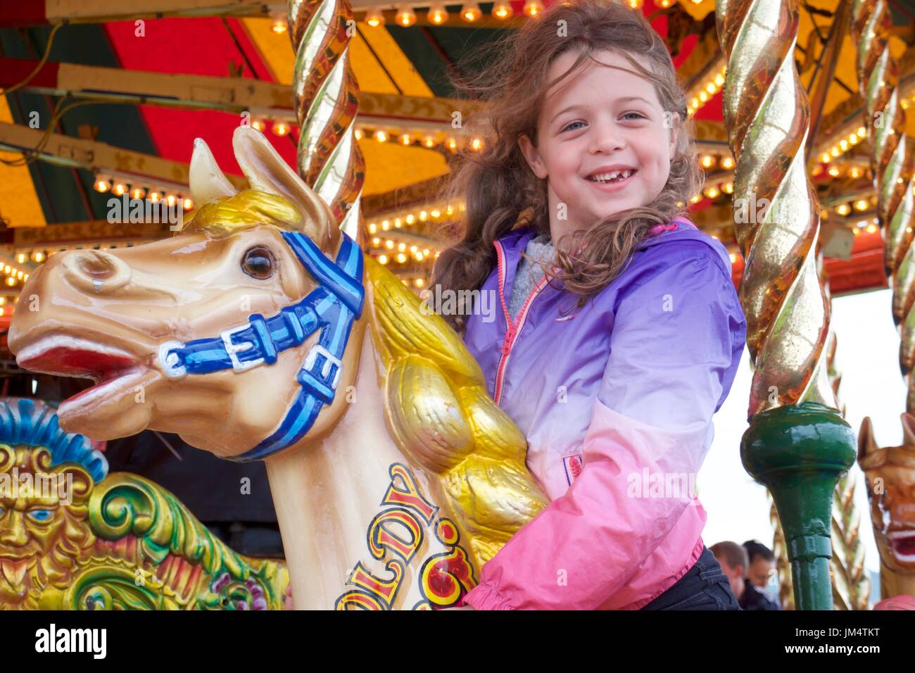 Happy girl riding fairground galloper horse at Masham Steam Fair, Masham, North Yorkshire, UK Stock Photo