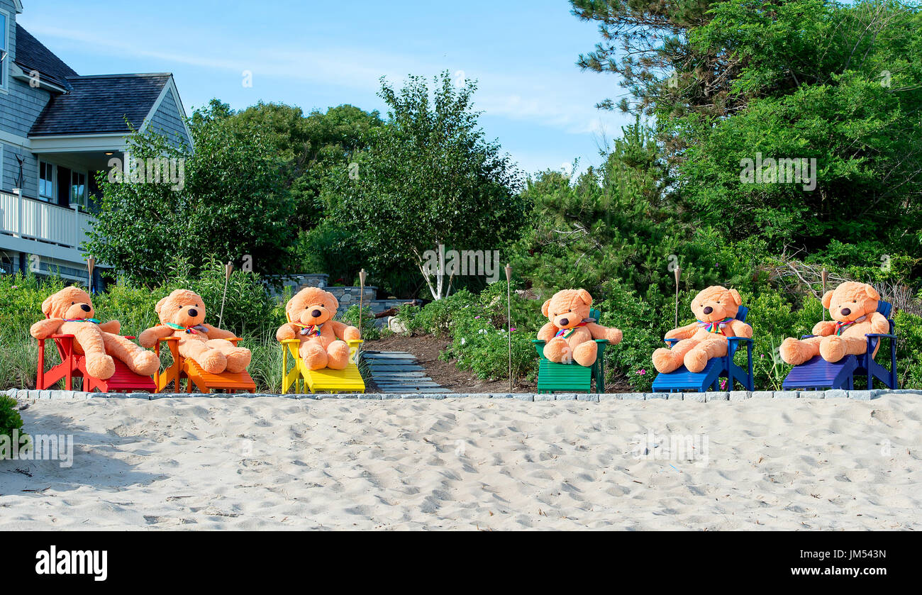 giant teddy bears seated in rainbow adirondack chairs on sandy beach front in Provincetown PTown MA Stock Photo