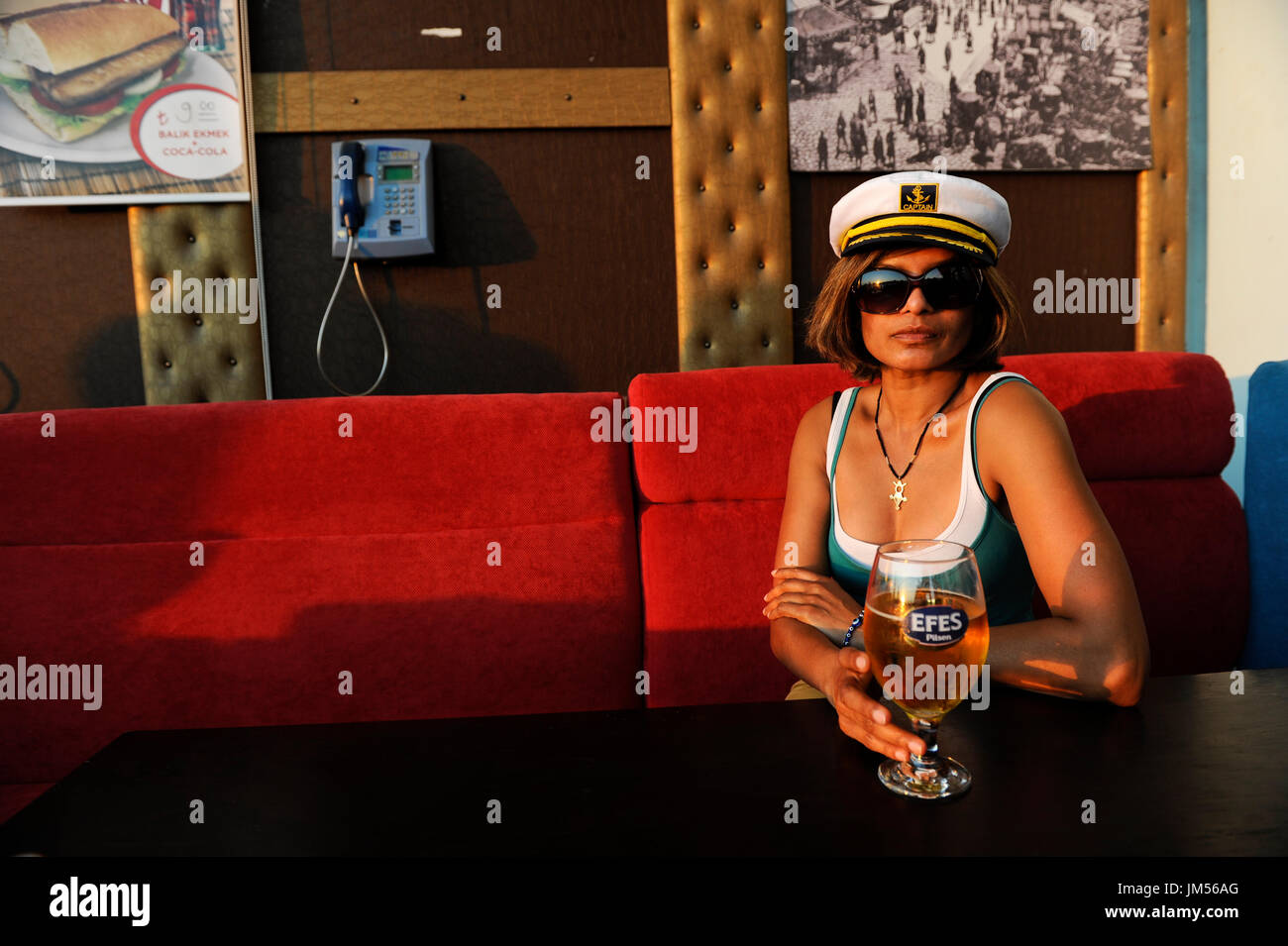TURKEY Istanbul, woman with captain hat drinks Efes beer in Pub under bridge over Golden Horn/ TUERKEI Istanbul, Frau mit Kapitaens Muetze trinkt Efes Bier Stock Photo