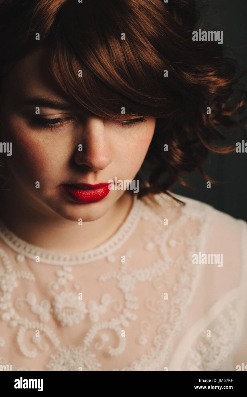 Young woman girl with brunette curly hair and red lips looking down and wearing a vintage white lace top Stock Photo