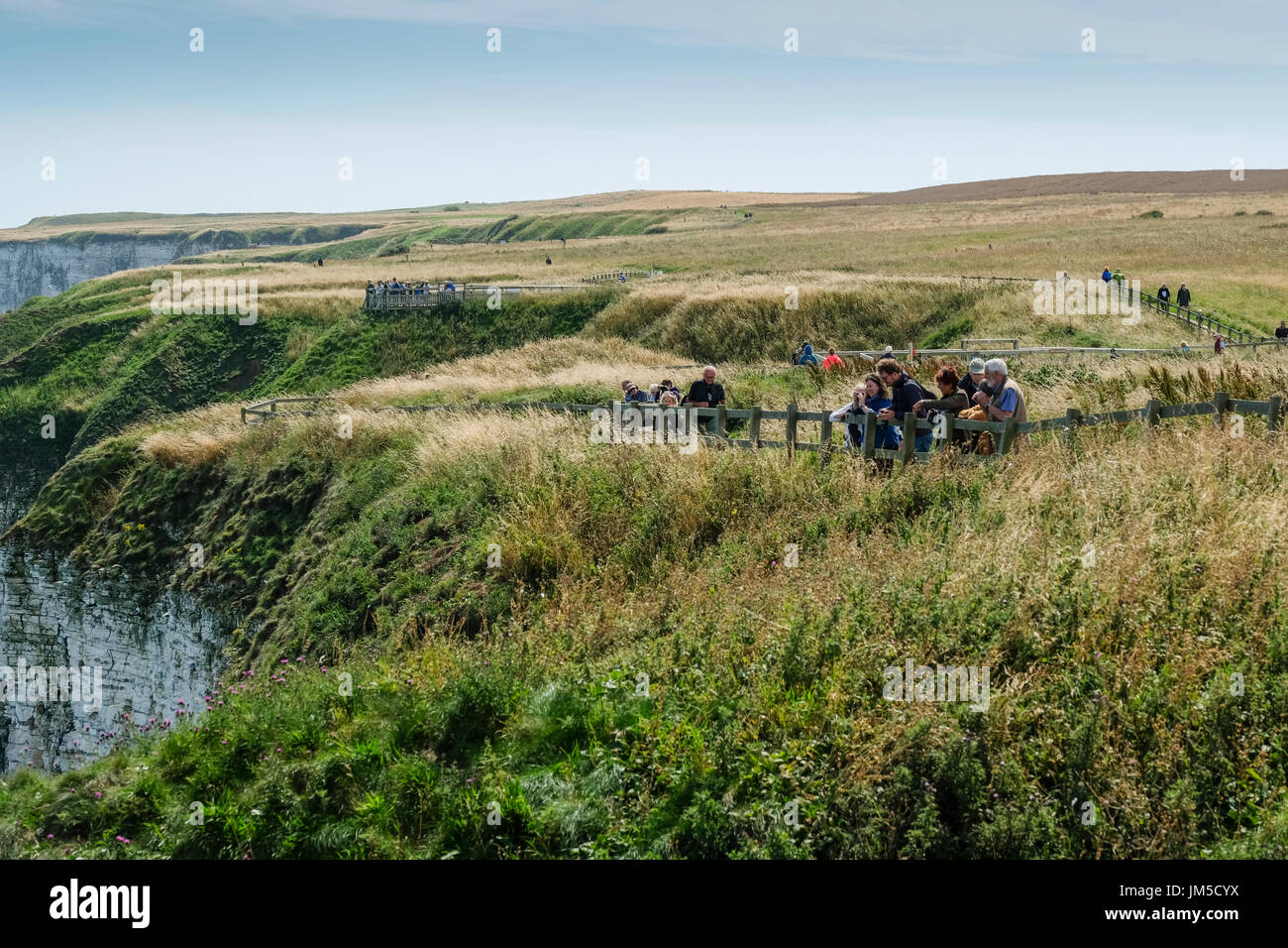 A group of people men and women males and females male and female bird watching at a viewpoint on the Bempton Cliffs RSPB Reserve, UK on a bright, sun. Stock Photo