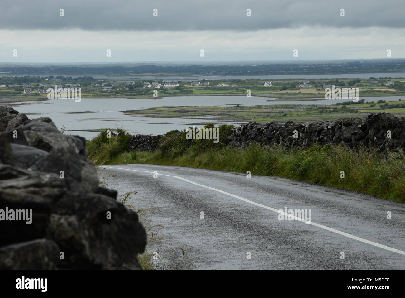 Asphalt road between the stone walls on the background of the Galway Bay in the County Clare, west Ireland Stock Photo
