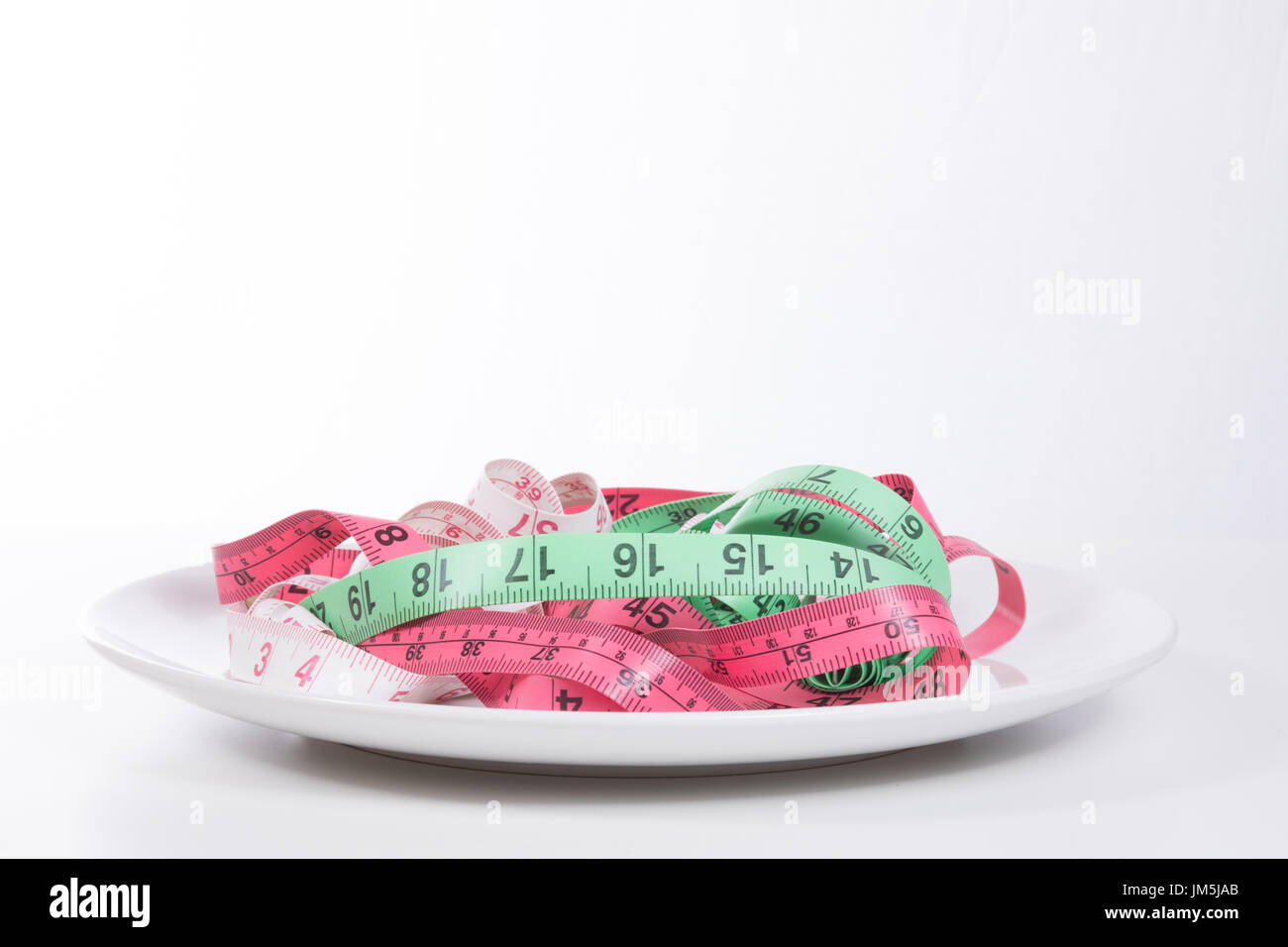 https://c8.alamy.com/comp/JM5JAB/plate-full-of-tangled-colored-measuring-tapes-viewed-from-the-side-JM5JAB.jpg