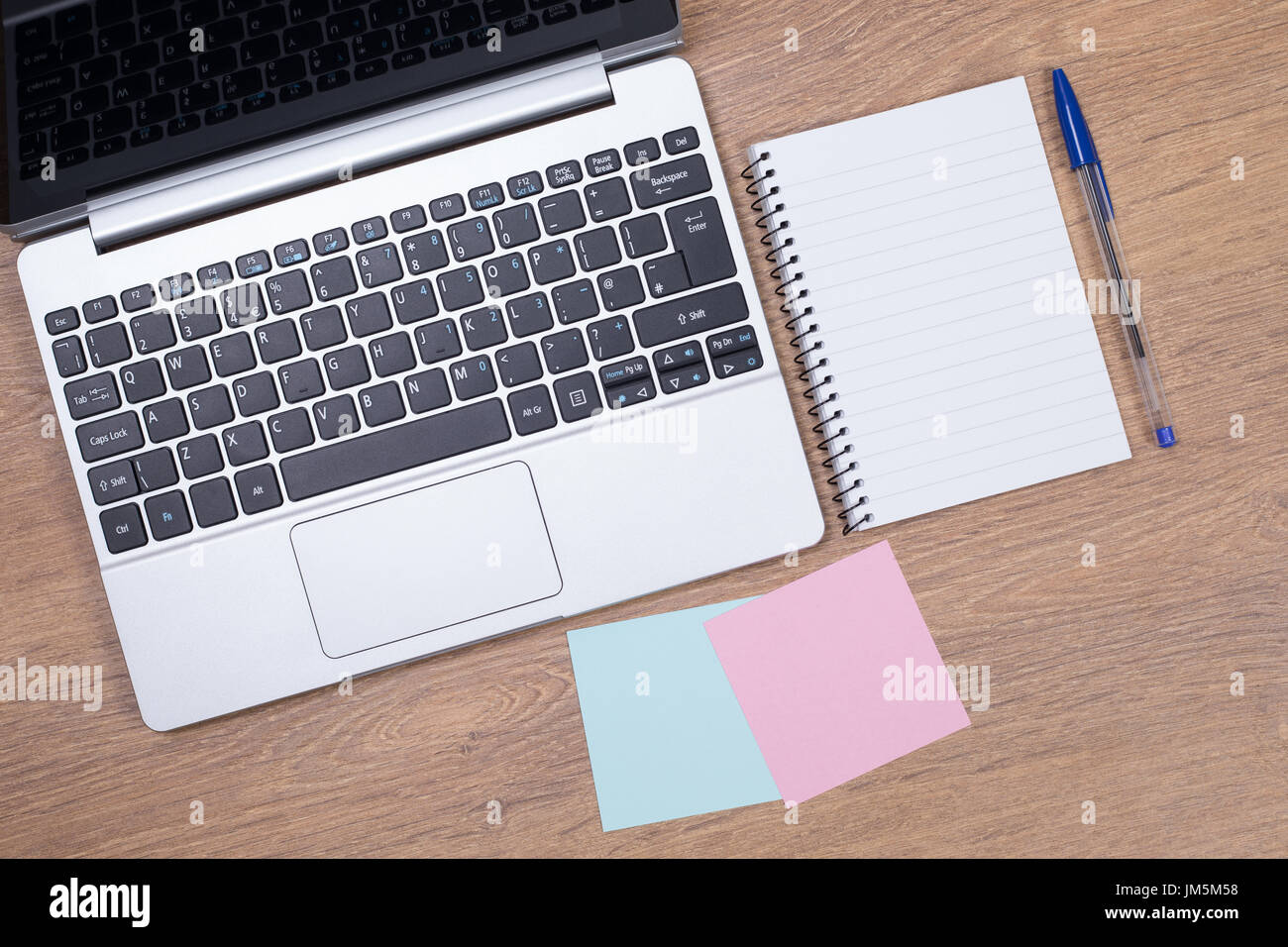 white lined note pad next to open laptop with sticky notes on a wooden surface Stock Photo
