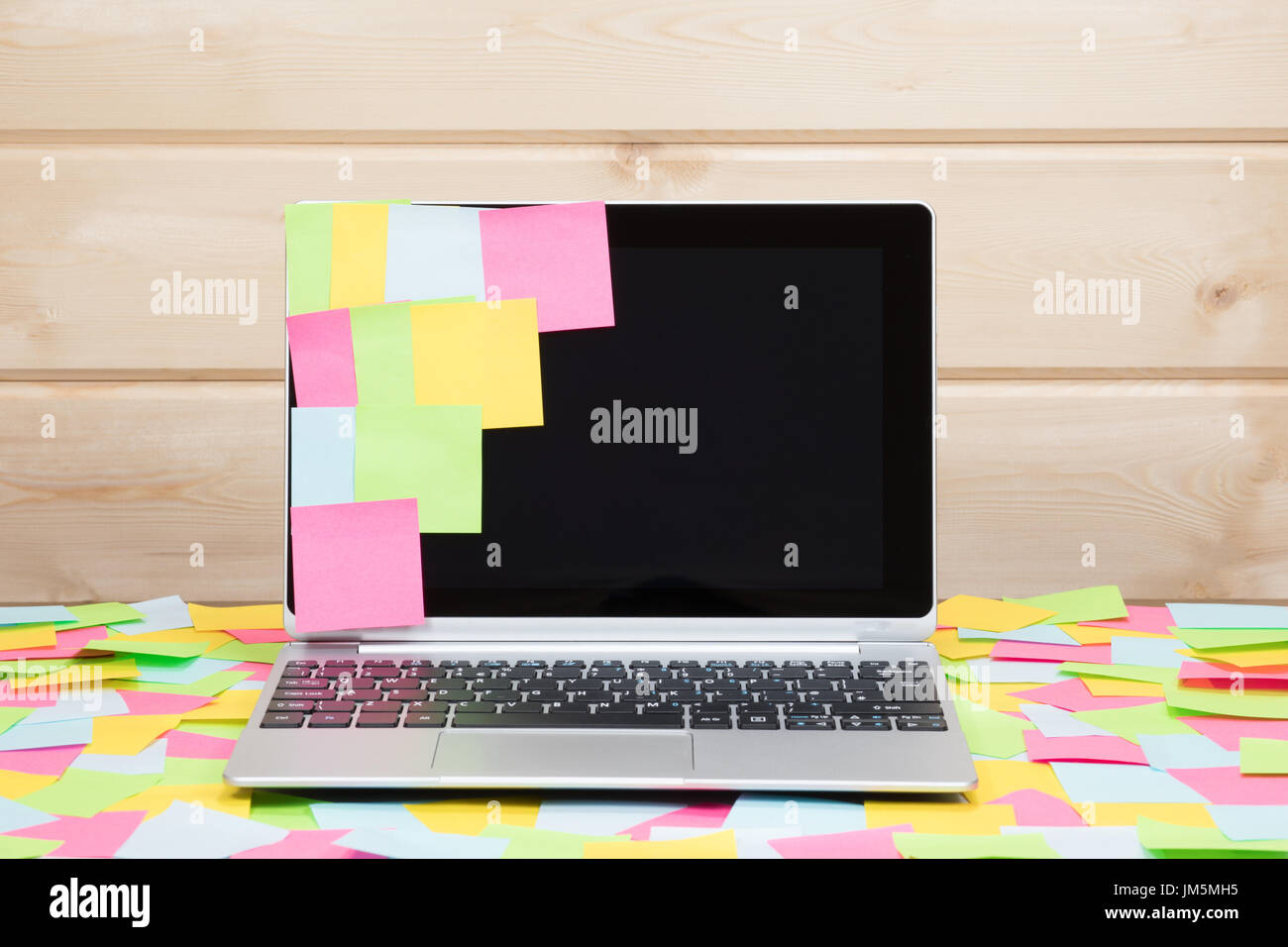Colorful blank sticky notes stuck to a laptop screen and scattered on the surrounding desk conceptual of reminders, multitasking and business schedule Stock Photo