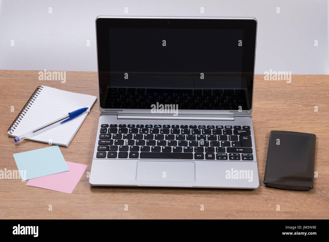 Neat workstation in an office with laptop computer and mobile phone together with blank memo notes and a spiral bound notepad and pen Stock Photo