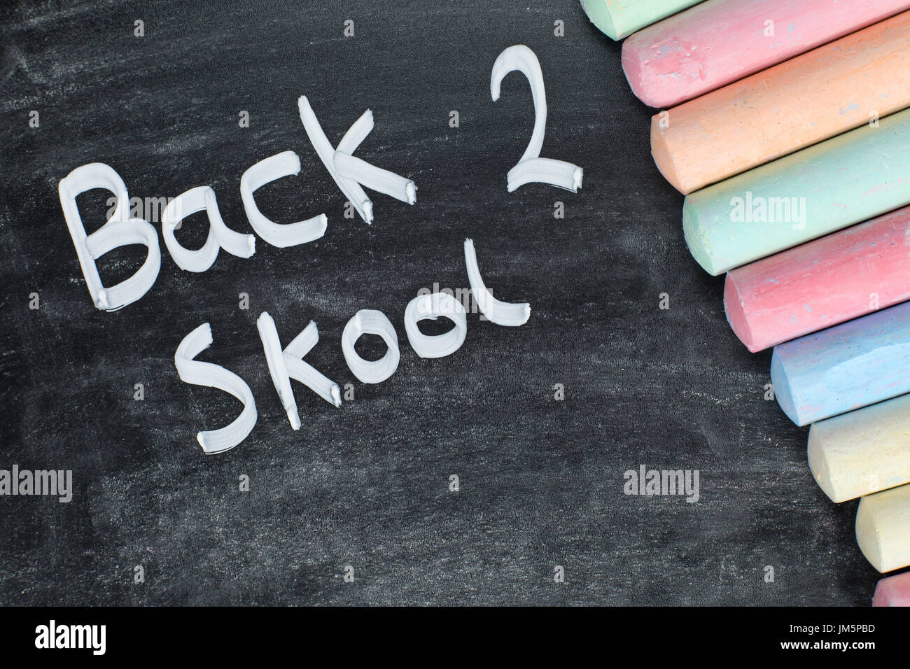 Misspelt Back 2 Skool concept with handwritten text on a textured chalkboard with a colorful border of chalk sticks and copy space Stock Photo
