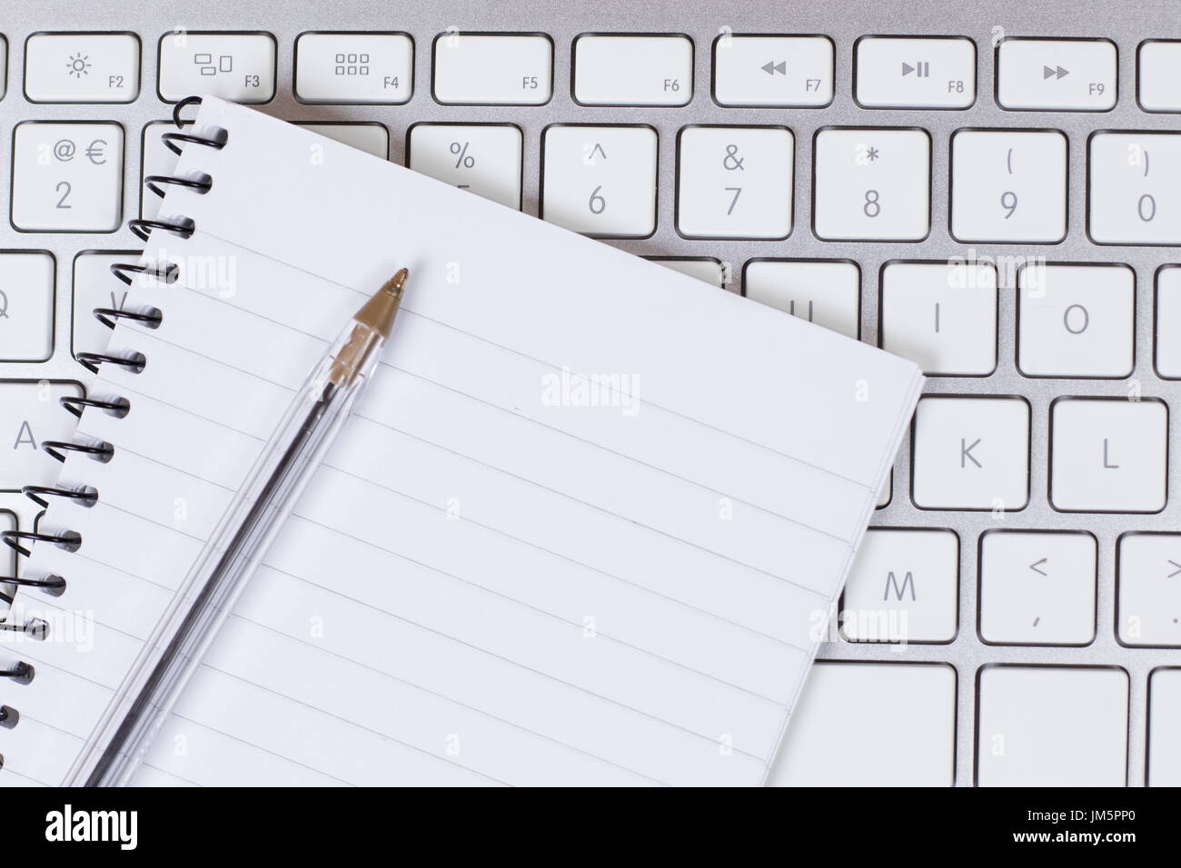 Business communication or learning concept with a blank notebook and ballpoint pen lying on the keyboard of an open laptop in a close up view Stock Photo