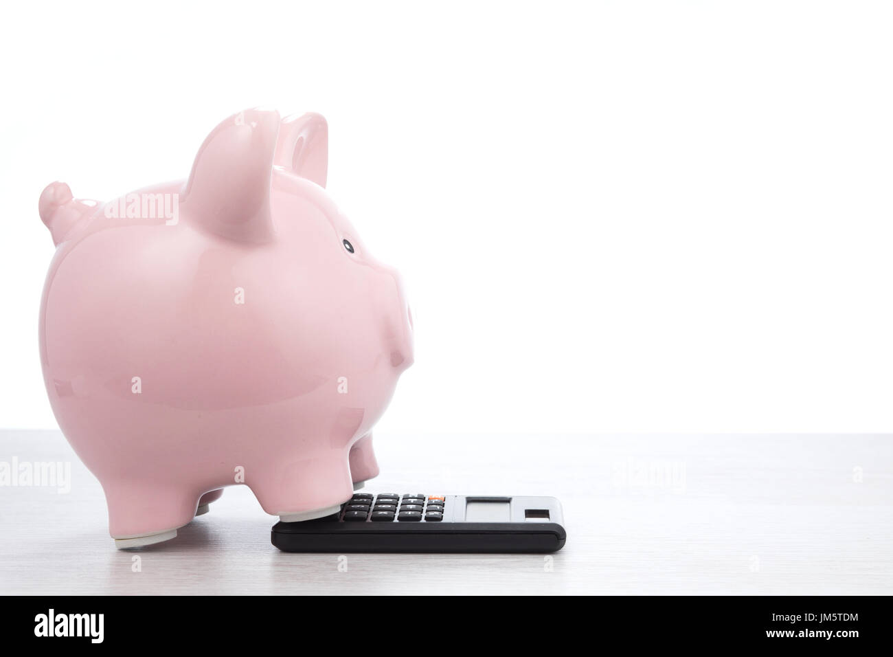 Fat little pink piggy standing bank on a calculator in a close up side ...