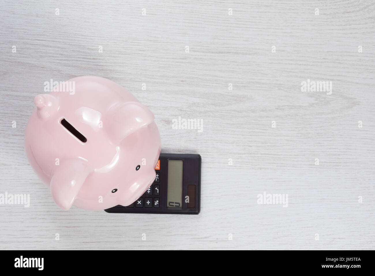 Pink piggy bank standing on a small manual calculator in a concept of ...