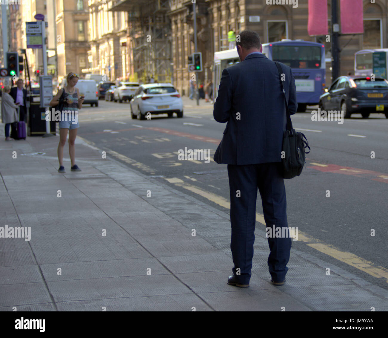 business man in suit on Glasgow George square texting mirrored by young woman in front of him Stock Photo