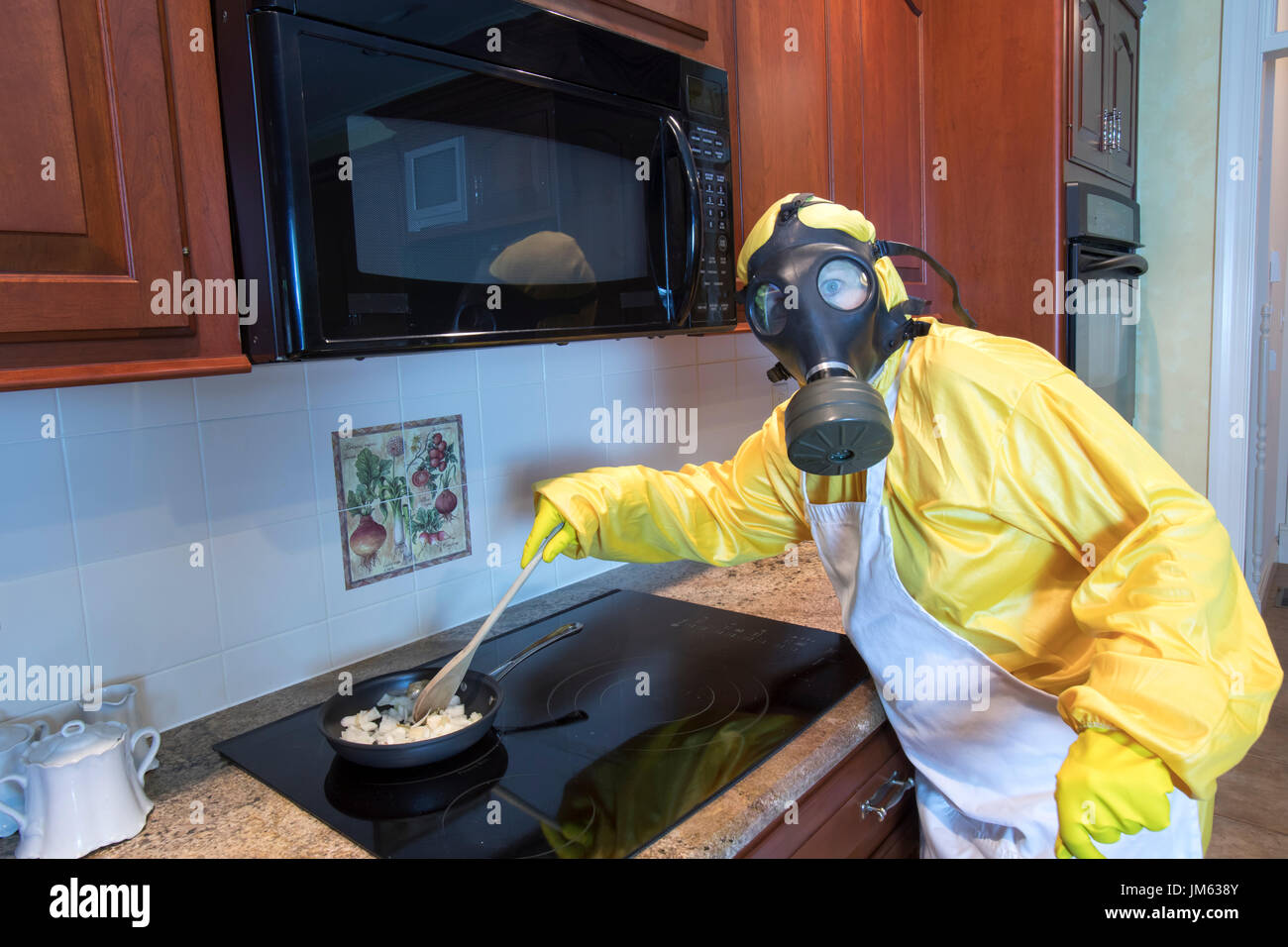 Mature woman in yellow Haz Mat suir and gas mask stirring onions in pan