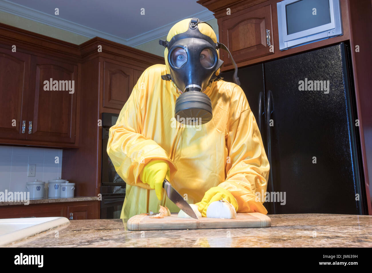 Mature woman in yellow Haz Mat suir and gas mask chopping onions in