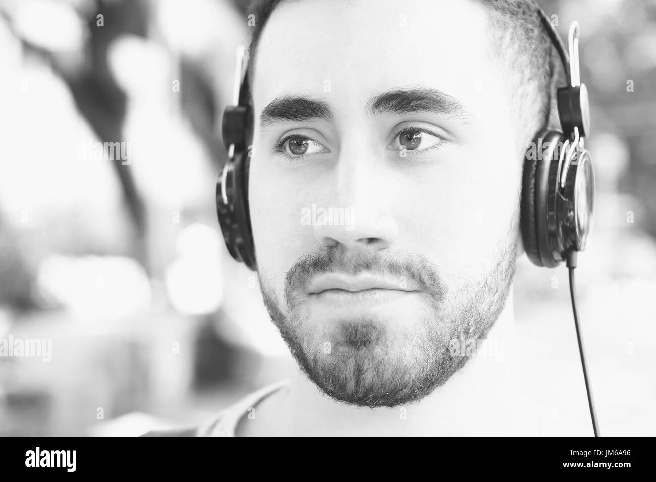 Portrait of young latin man listening to music with black headphones. Outdoors. Stock Photo