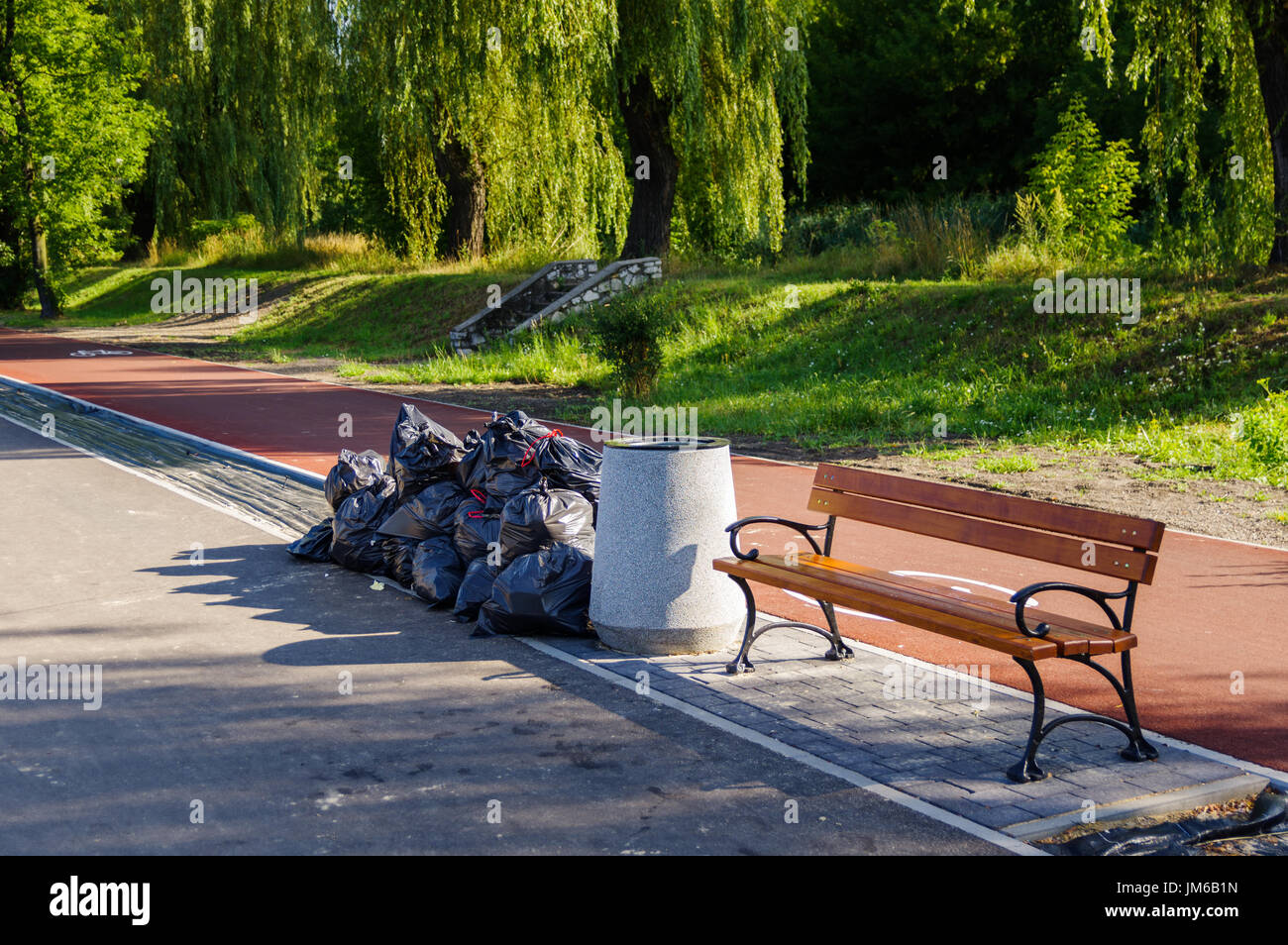 Park bench with trashcan and black trash bags at Stawiki in Sosnowiec, Poland Stock Photo