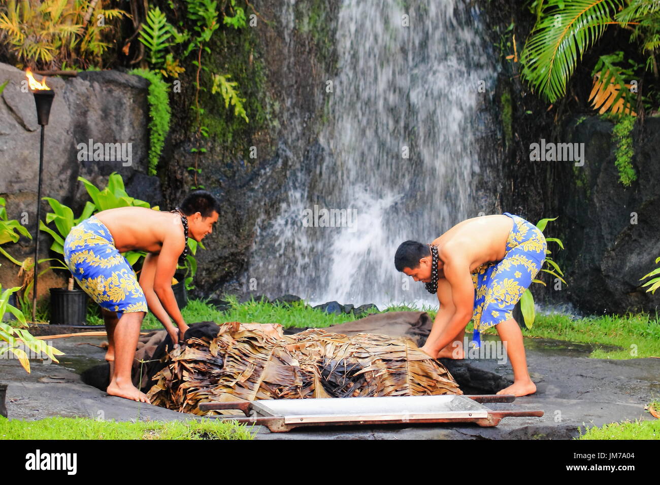 Honolulu, Hawaii - May 27, 2016: Two young Hawaiian men at the Polynesian Cultural Center uplift a pig cooked in the traditional style Kalua utilizing Stock Photo