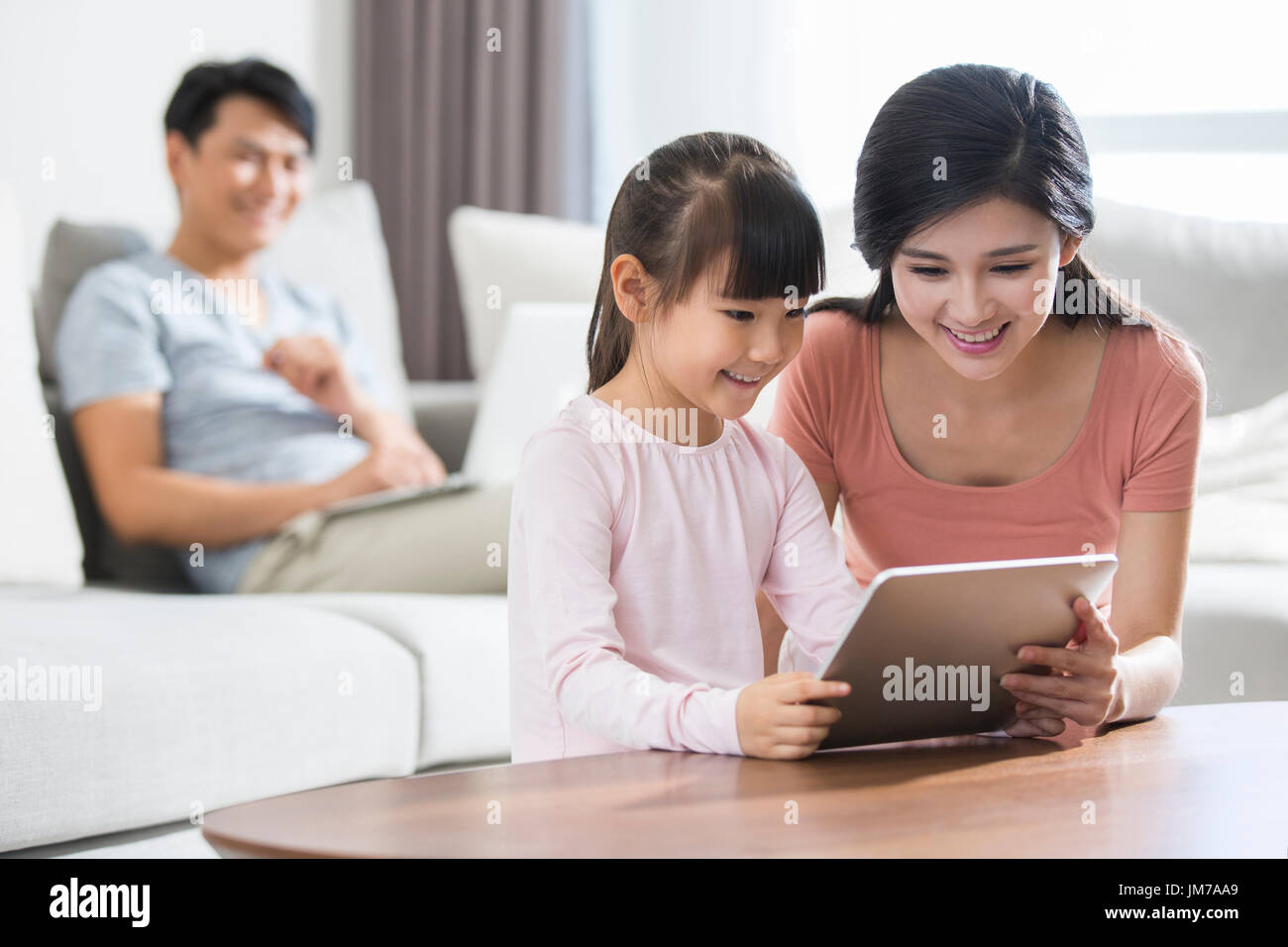 Happy young Chinese family using digital gadgets at home Stock