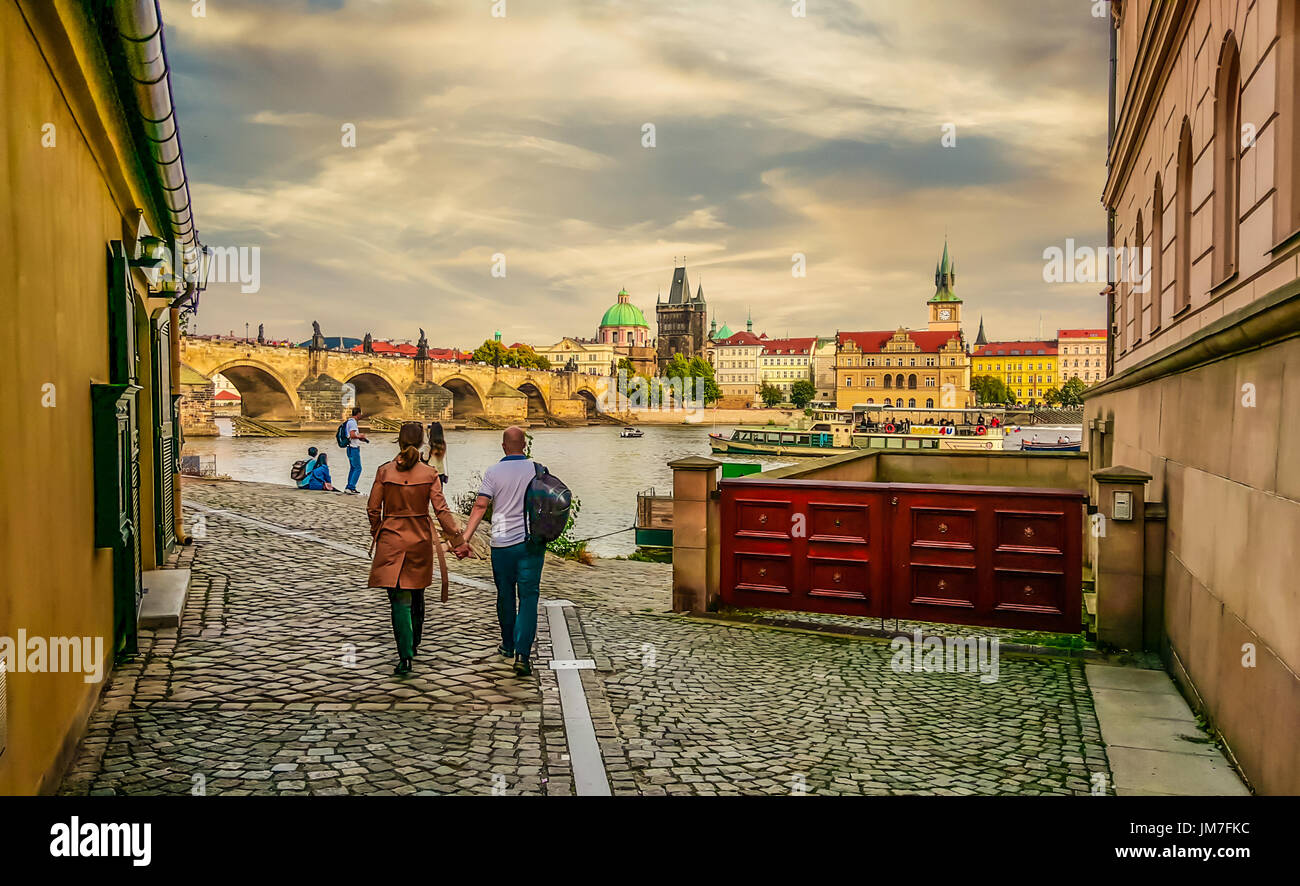 A couple walks toward the riverbank and Charles Bridge in Prague on an overcast Autumn day Stock Photo