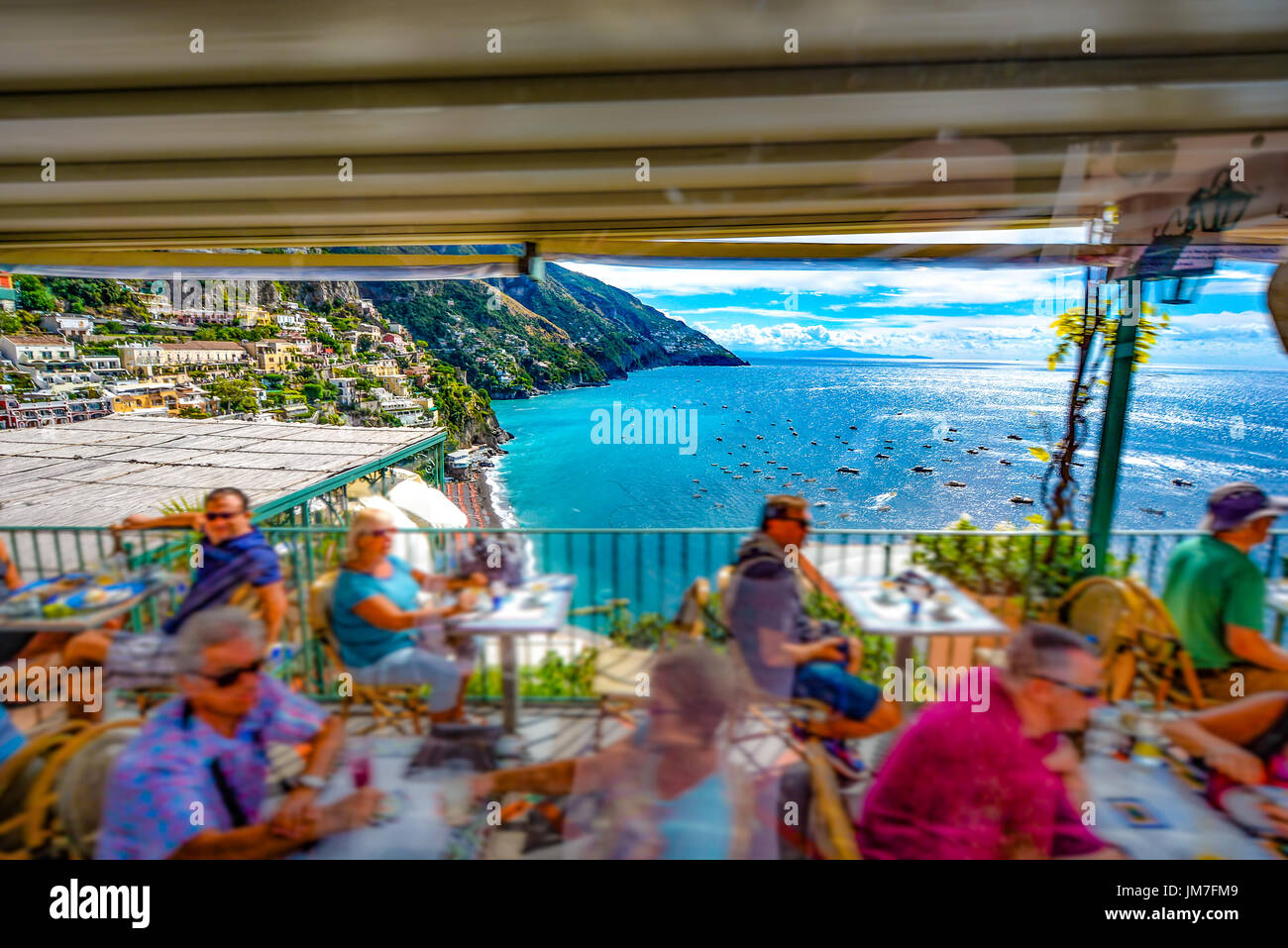 Driving by a cliffside restaurant with tourists dining as they overlook the beautiful Amalfi coast and hillside town in Italy Stock Photo