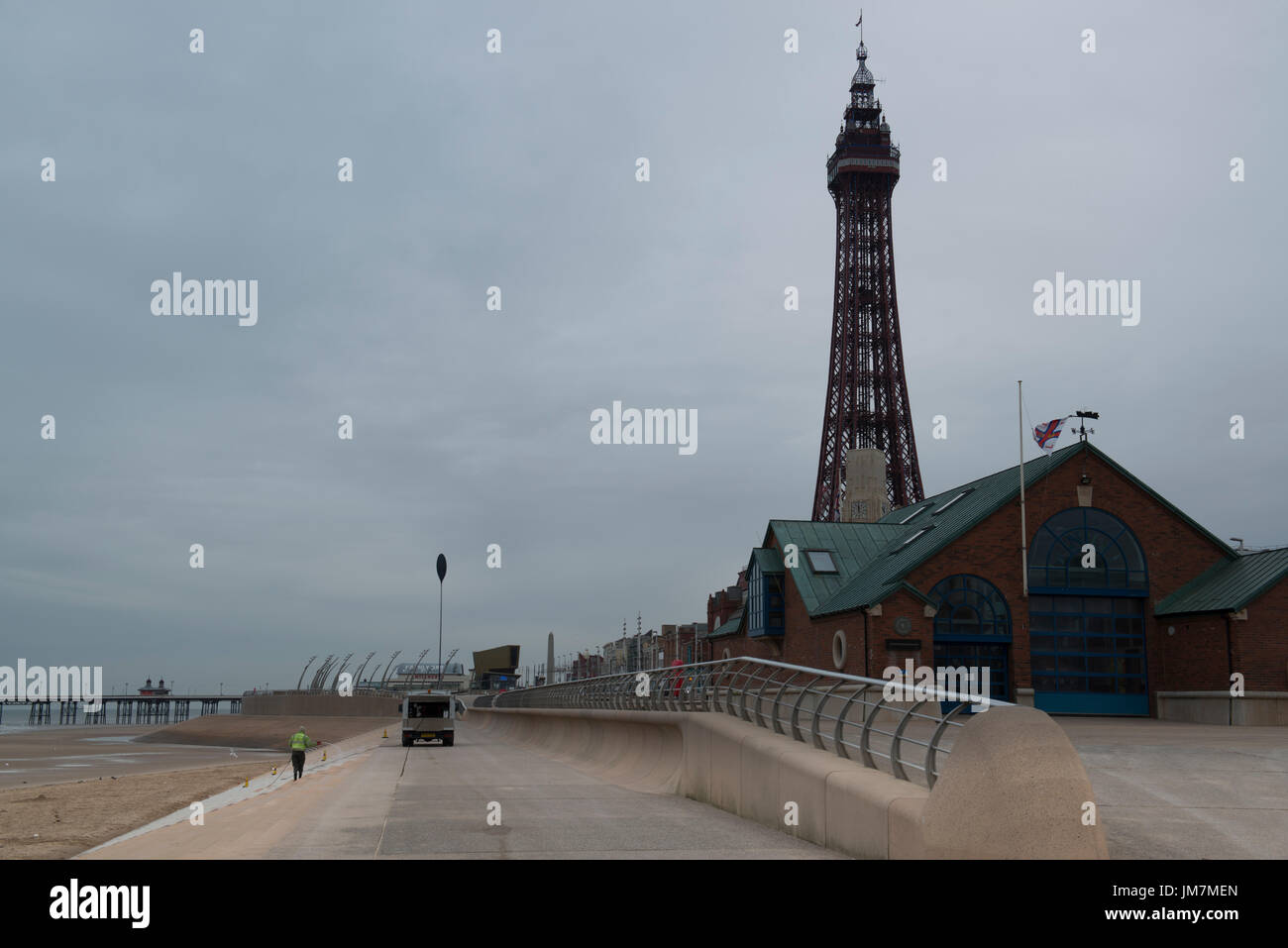 Fylde borough council employee, pressure washing sea front, with Blackpool tower in the background. credit: LEE RAMSDEN / ALAMY Stock Photo