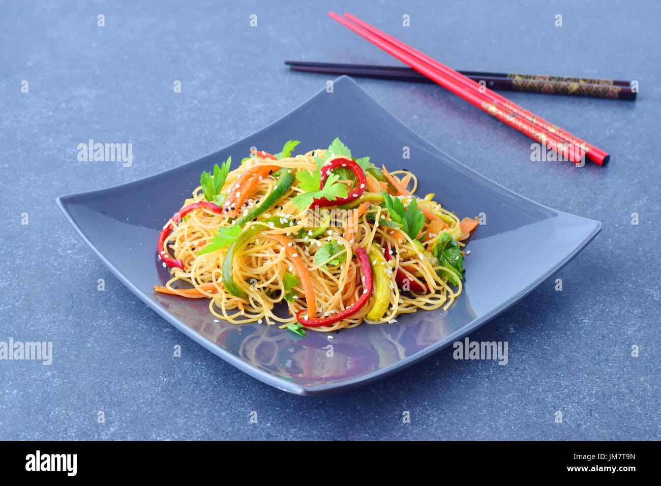 A grey ceramic plate with noodles and vegetables on a grey abstract background. Asian food. Healthy eating concept Stock Photo