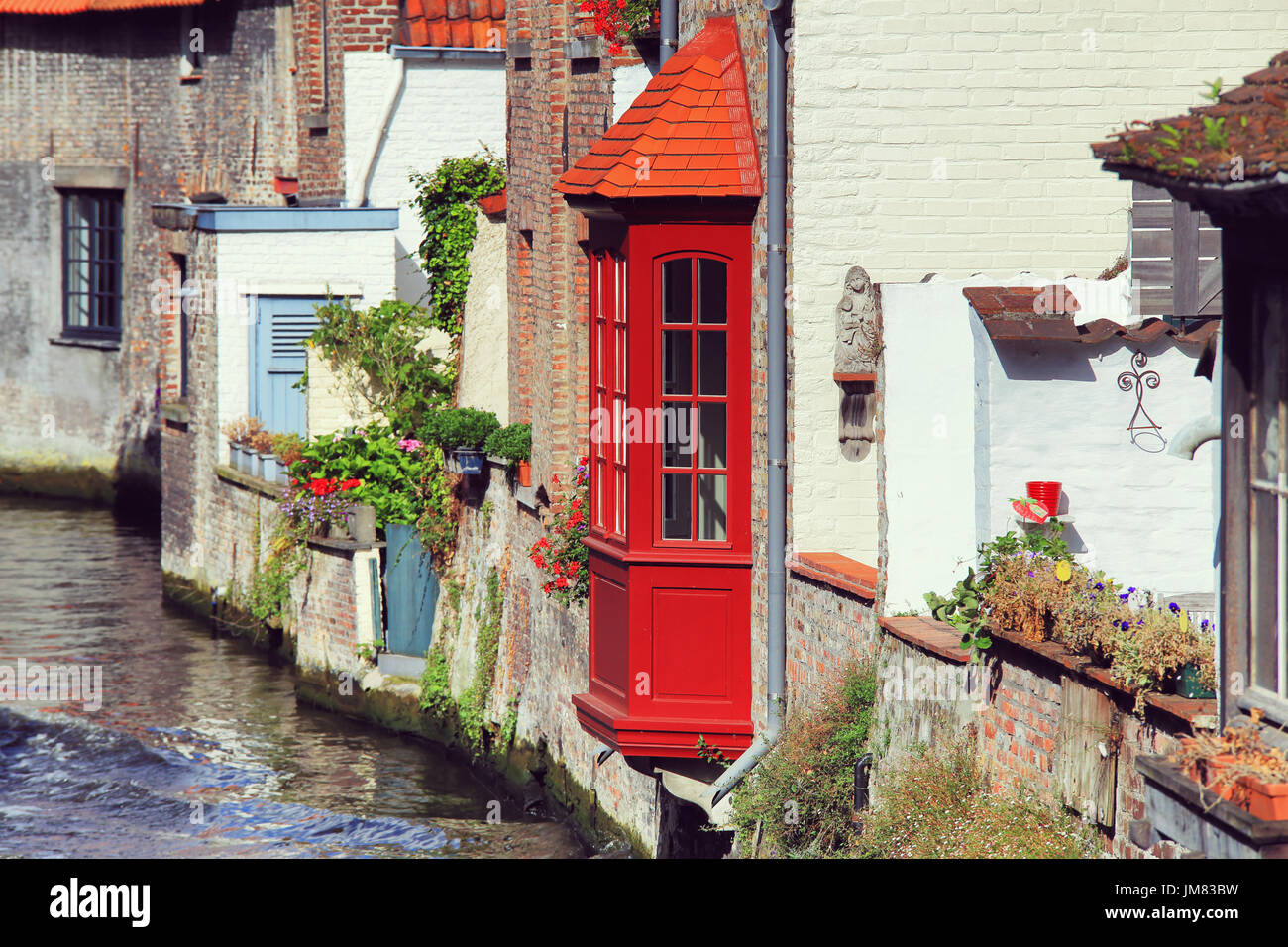 River view to old walls of Bruges buildings. Red bow window over water channel in Bruges. Stock Photo