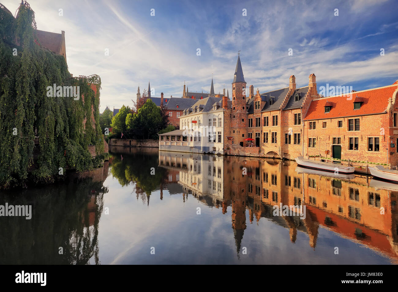 Historical centre of Bruges  in the evening sunlight. Bruges river view. Old Bruges buildings reflecting in water canal. Vibrant blue sky over Belgium Stock Photo