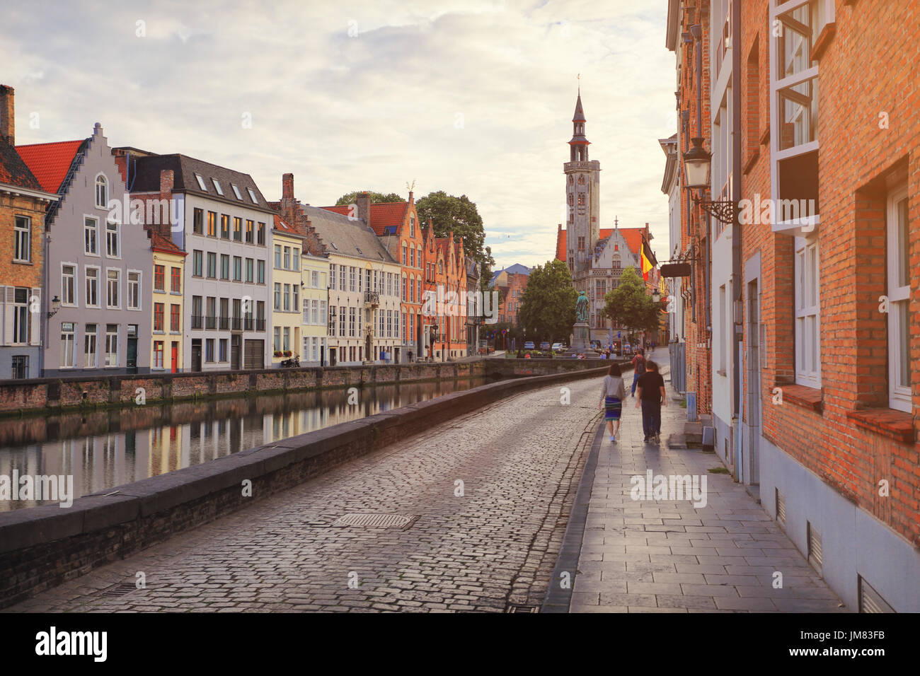 Bruges, Belgium. Retro road along water canal in Bruges. Bruges road from paving stones in historic town centre. Stock Photo