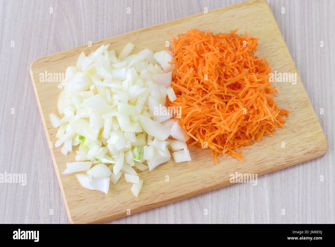 Step by step cooking. Cut onion and carrots on a wooden cutting board on a wooden background. Stock Photo