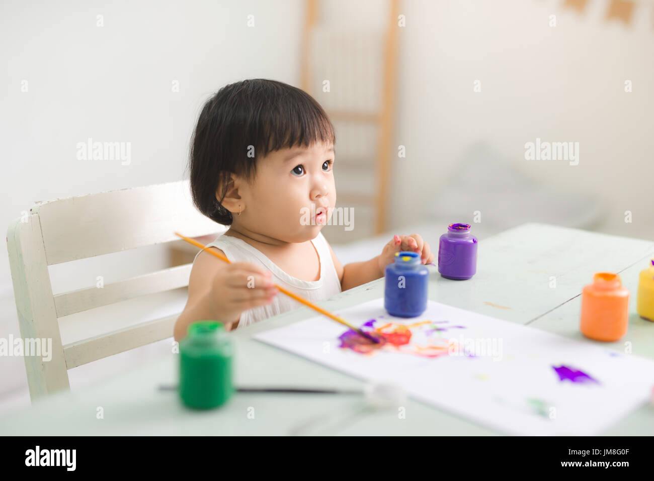 Funny laughing asian baby girl drawing with colorful pencils at home Stock Photo