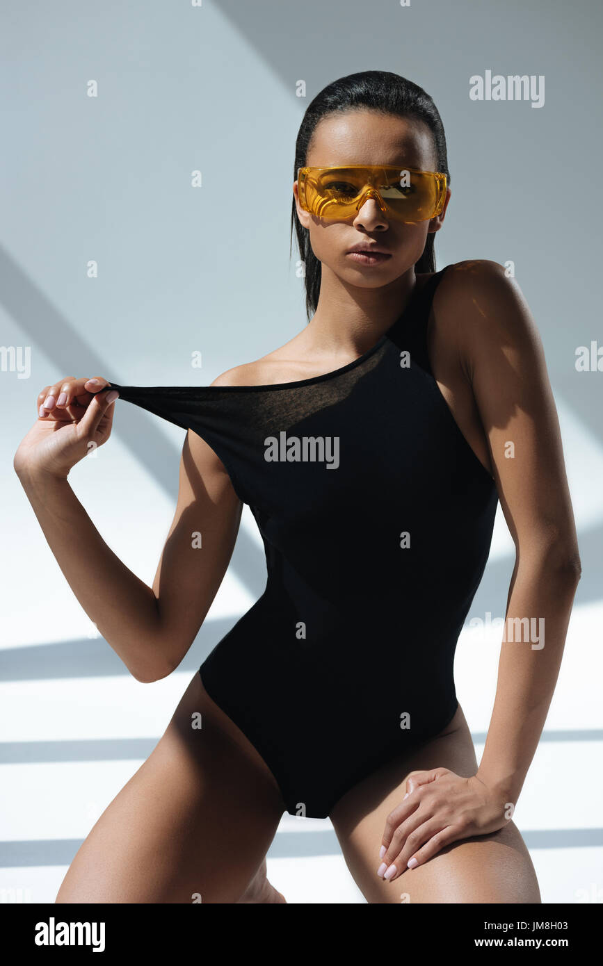 african american stylish model in black swimsuit and protective goggles  posing on grey and looking at camera Stock Photo - Alamy