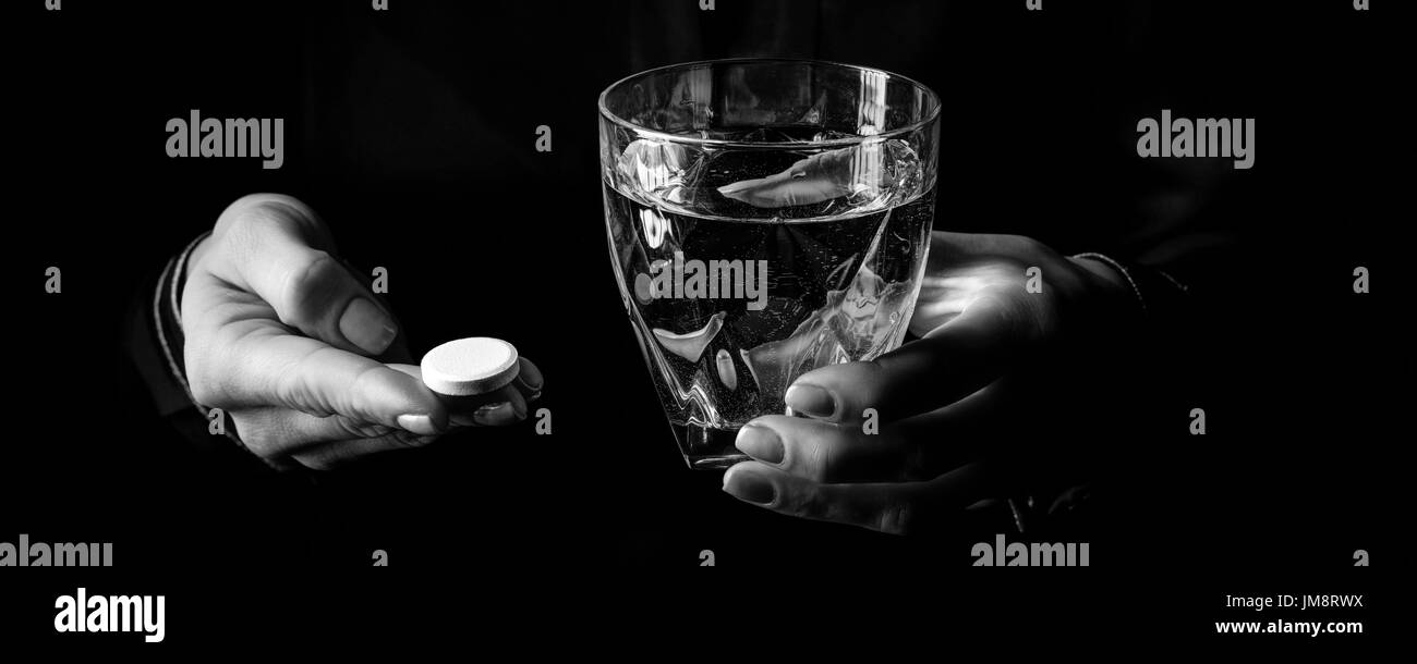 Black Mania. female hands isolated on black showing pill and glass of water Stock Photo