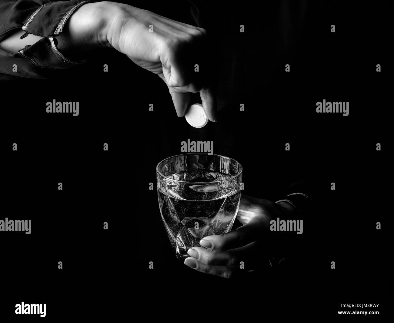 Black Mania. female hands isolated on black background showing effervescent tablet and glass of water Stock Photo