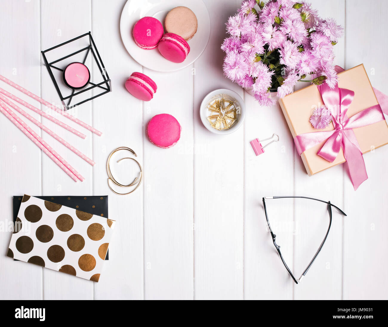 Pink flowers, macarons, candle, glasses and other cute small feminine accessories on the white wooden table Stock Photo