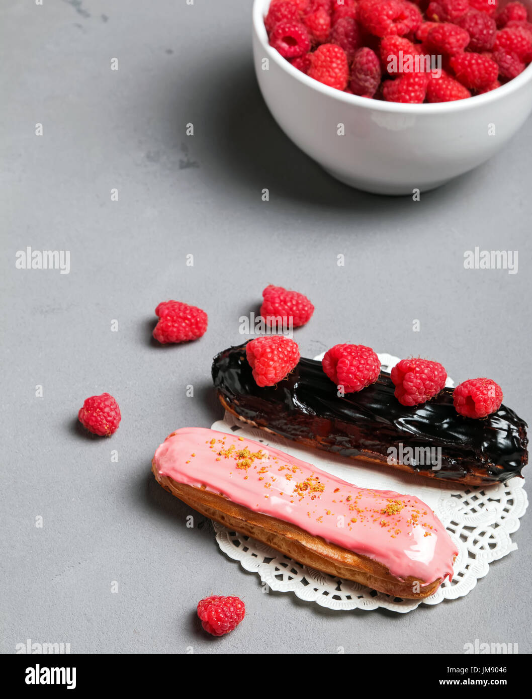 Delicious eclairs with glaze and fresh raspberries for decorating close-up Stock Photo