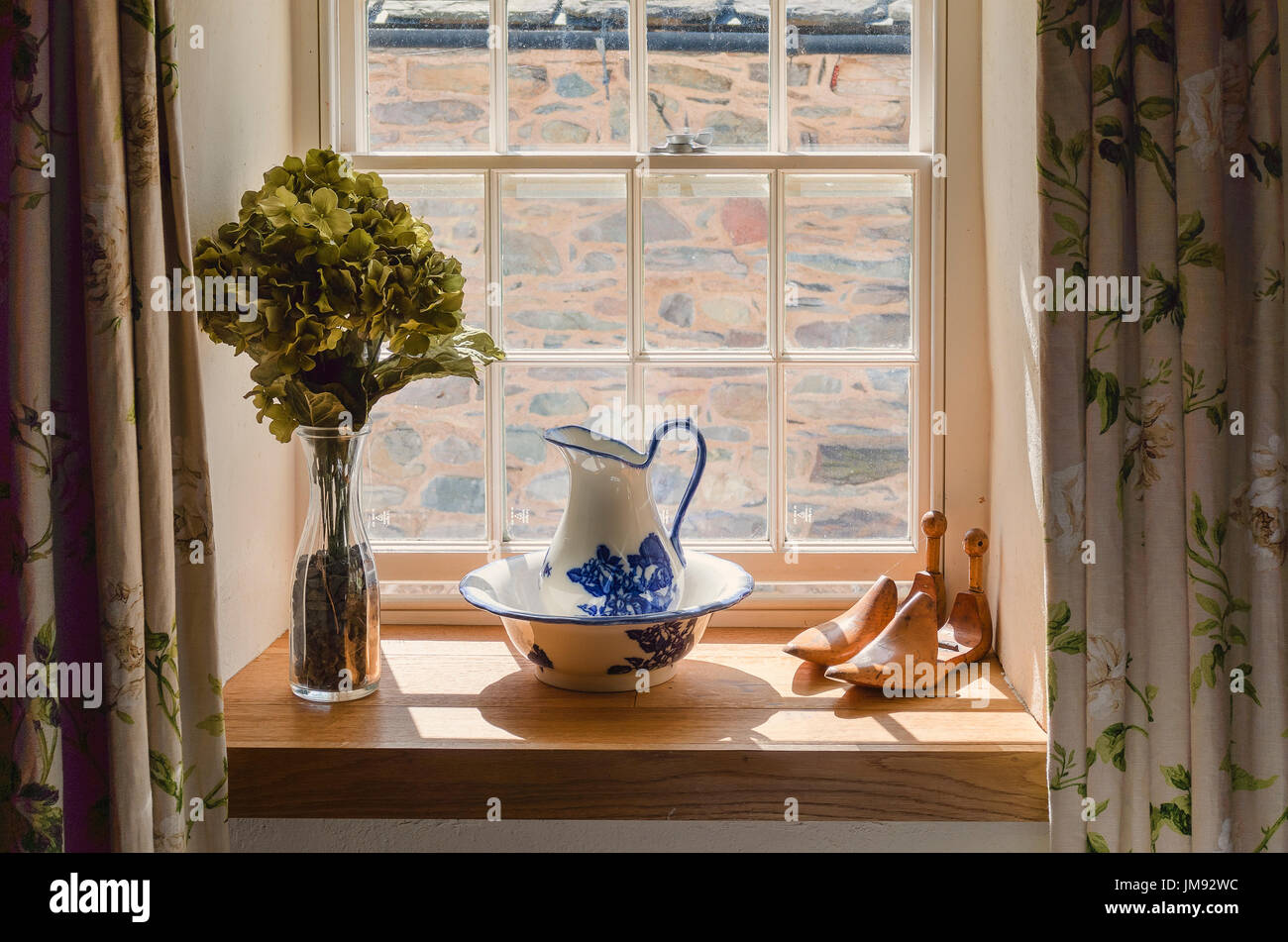 Still life window decor in a Cumbrian holiday home UK showing old washing bowl and a pair of wooden lasts Stock Photo