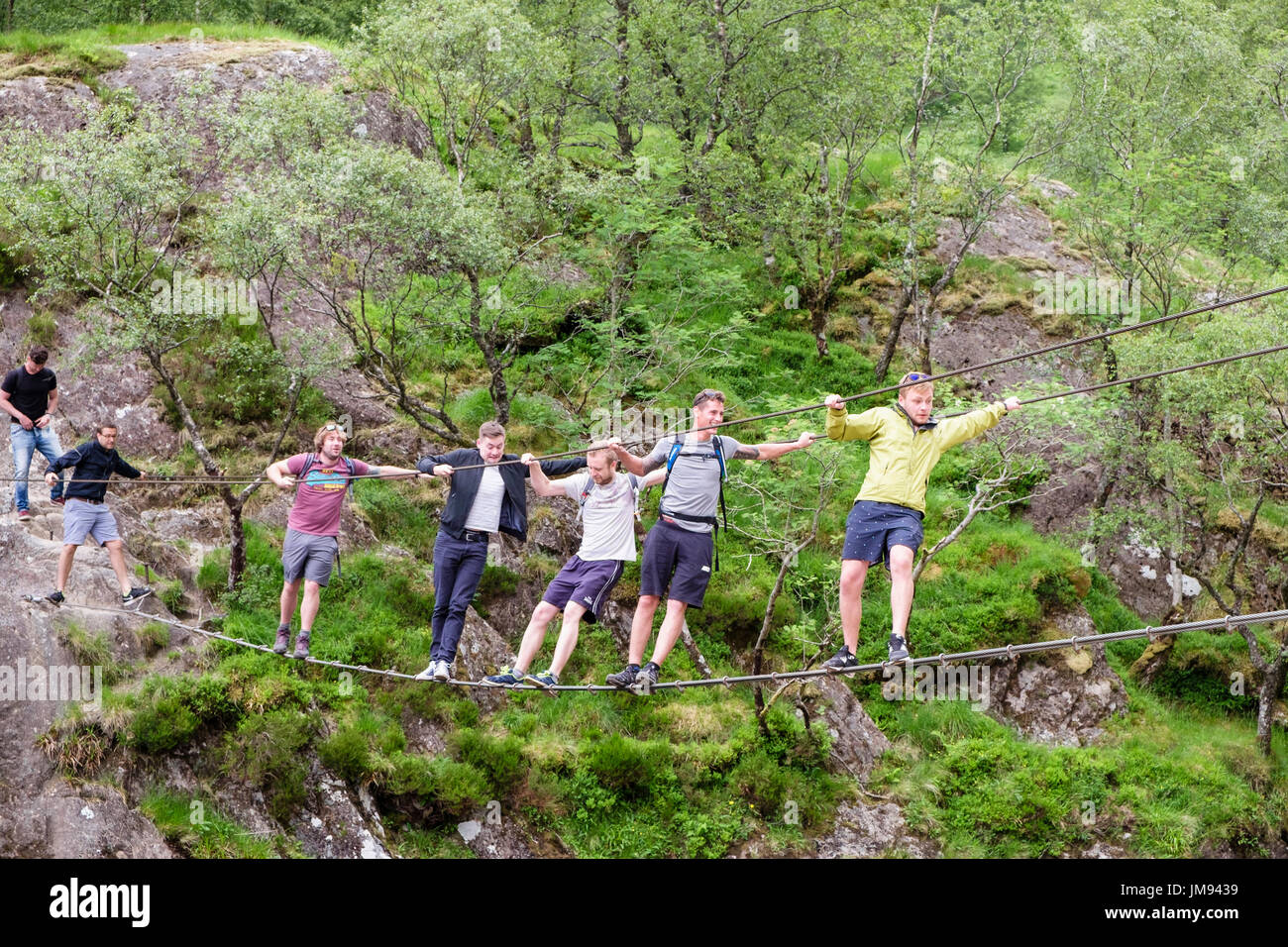 Six men messing about swinging on Steall wire bridge crossing Water of Nevis river. Glen Nevis, Fort Willaim, Highland, Scotland, UK, Britain Stock Photo