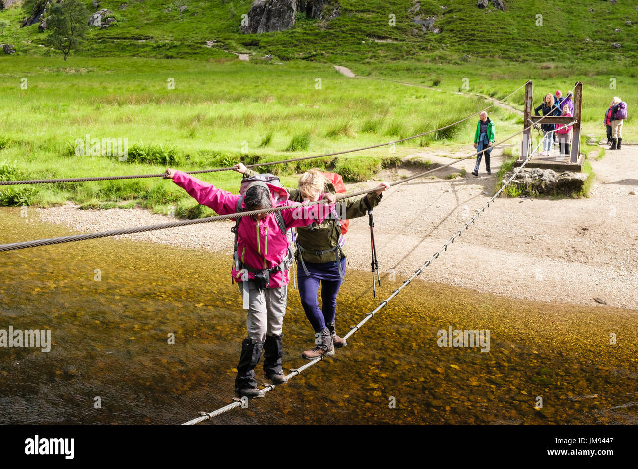 Two women hikers walking across Steall wire bridge crossing Water of Nevis river. Glen Nevis, Fort Willaim, Lochabar, Highland, Scotland, UK, Britain Stock Photo