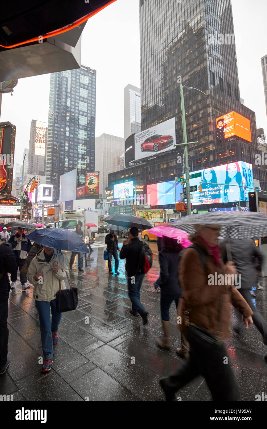 people carrying umbrellas walking past times square in a hurry in the rain New York City USA Stock Photo