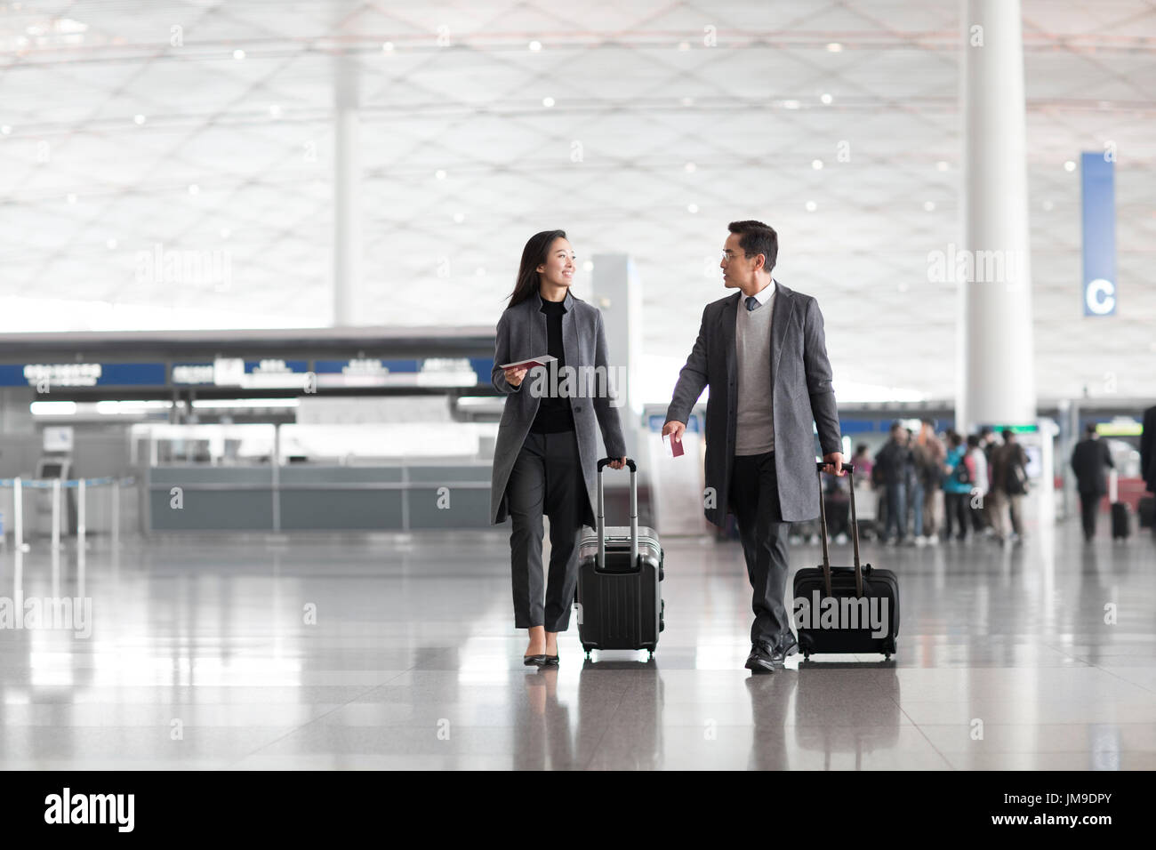 Chinese business people pulling wheeled luggage in airport lobby Stock
