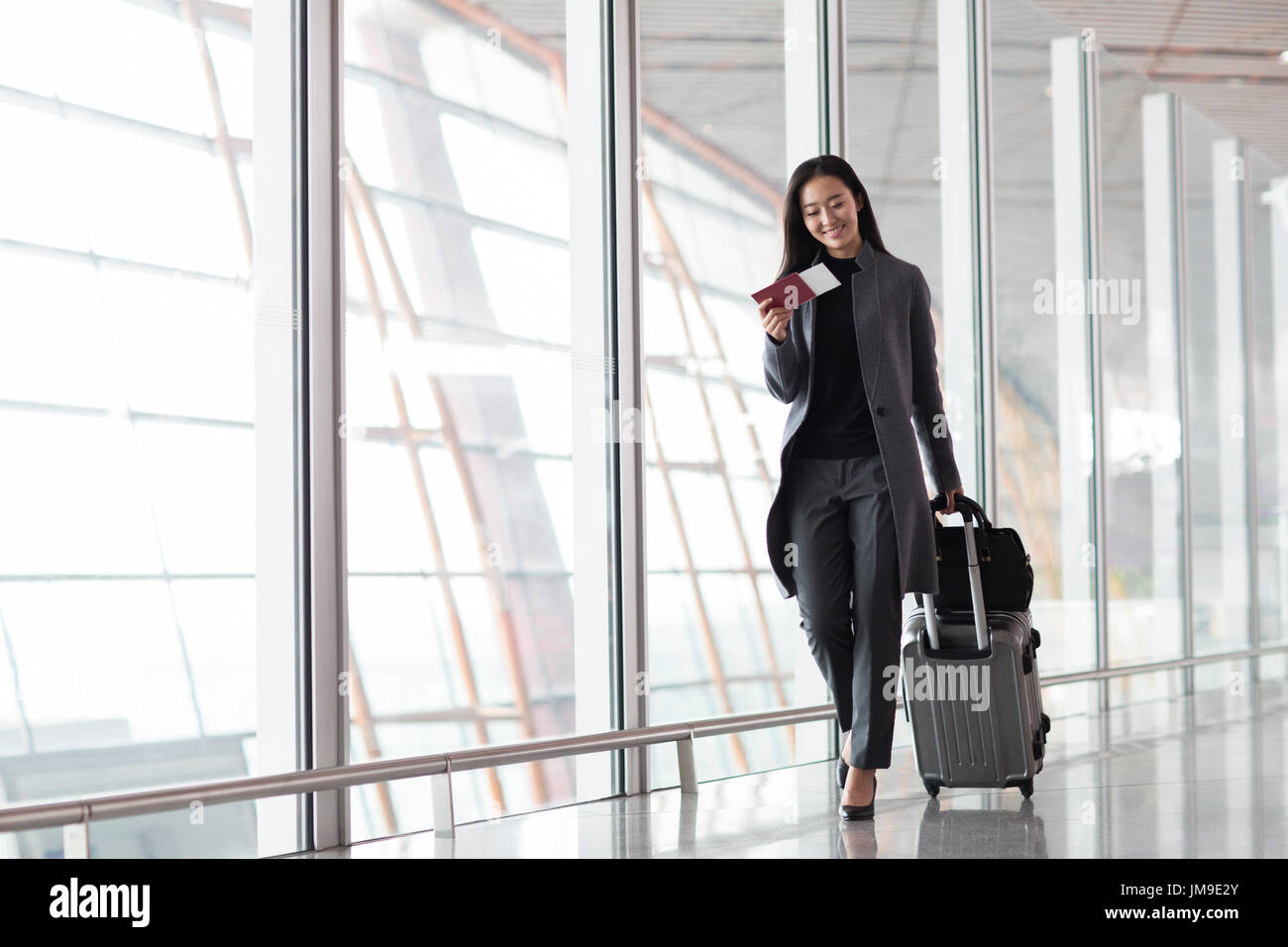Chinese businesswoman pulling wheeled luggage in airport lobby Stock