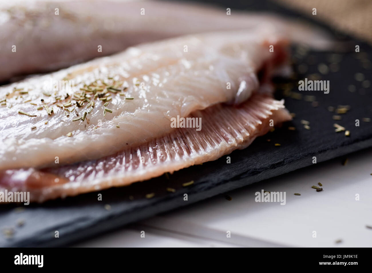closeup of a pair of raw filleted common sole on a slate tray placed on a rustic wooden table Stock Photo