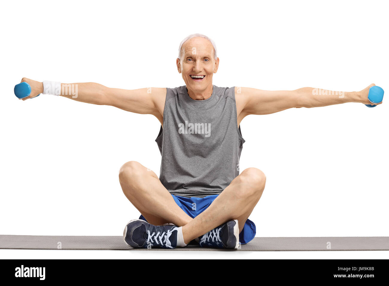 Elderly man lifting dumbbells and sitting on an exercise mat isolated on white background Stock Photo