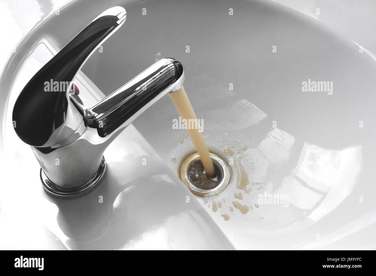 Water tap faucet with flowing contaminated muddy and dirty water in a white bathroom sink. Stock Photo