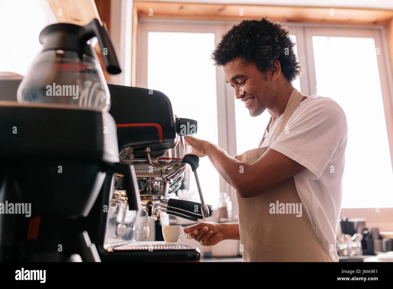 Professional barista holding cup on the coffee machine. Young man making coffee with an espresso coffee machine at cafe. Stock Photo