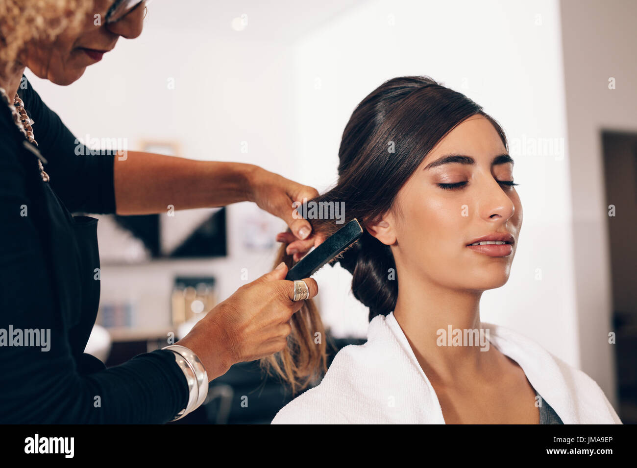 Woman hairdresser using a hairbrush for a hairdo at the salon. Young woman getting a stylish hairdo done at salon. Stock Photo