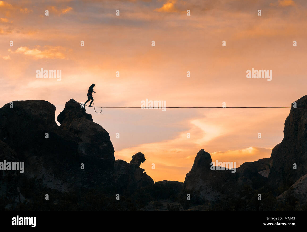 An acrobat walking the slackline between two mountains at dusk with an
