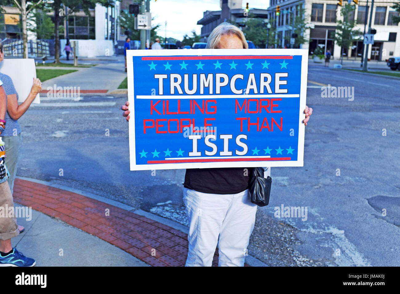 Youngstown, Ohio, USA. 25th July, 2017. Female protester stands on a street corner demonstrating against Trumpcare, the healthcare bill initiative, during a visit to the city by President Trump. Credit: Mark Kanning/Alamy Live News Stock Photo