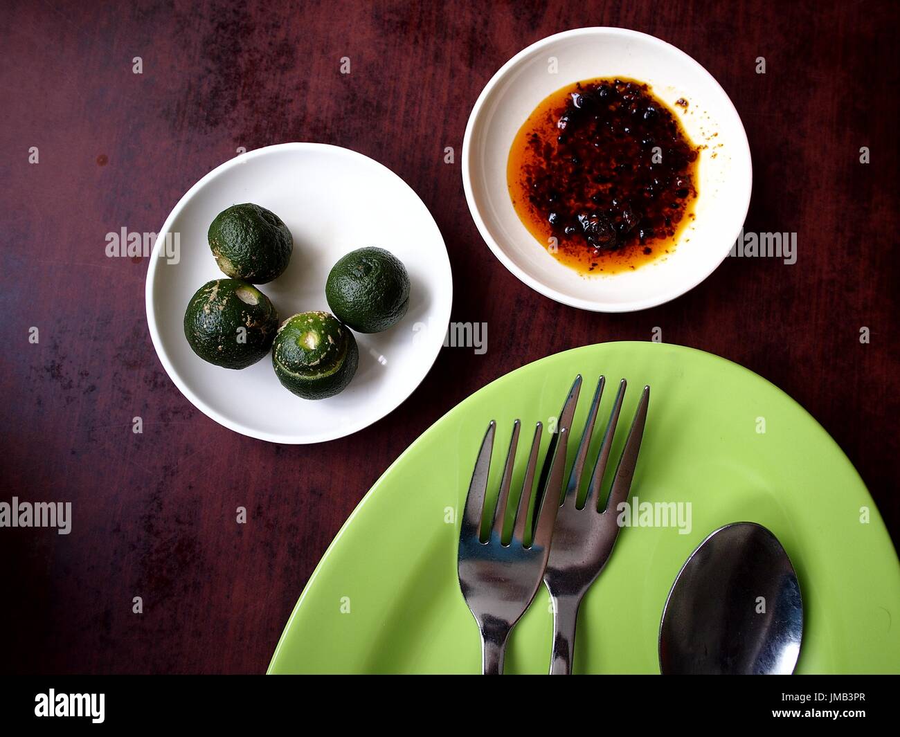 Top shot of green plate, utensils, chilli sauce and calamansi Stock Photo