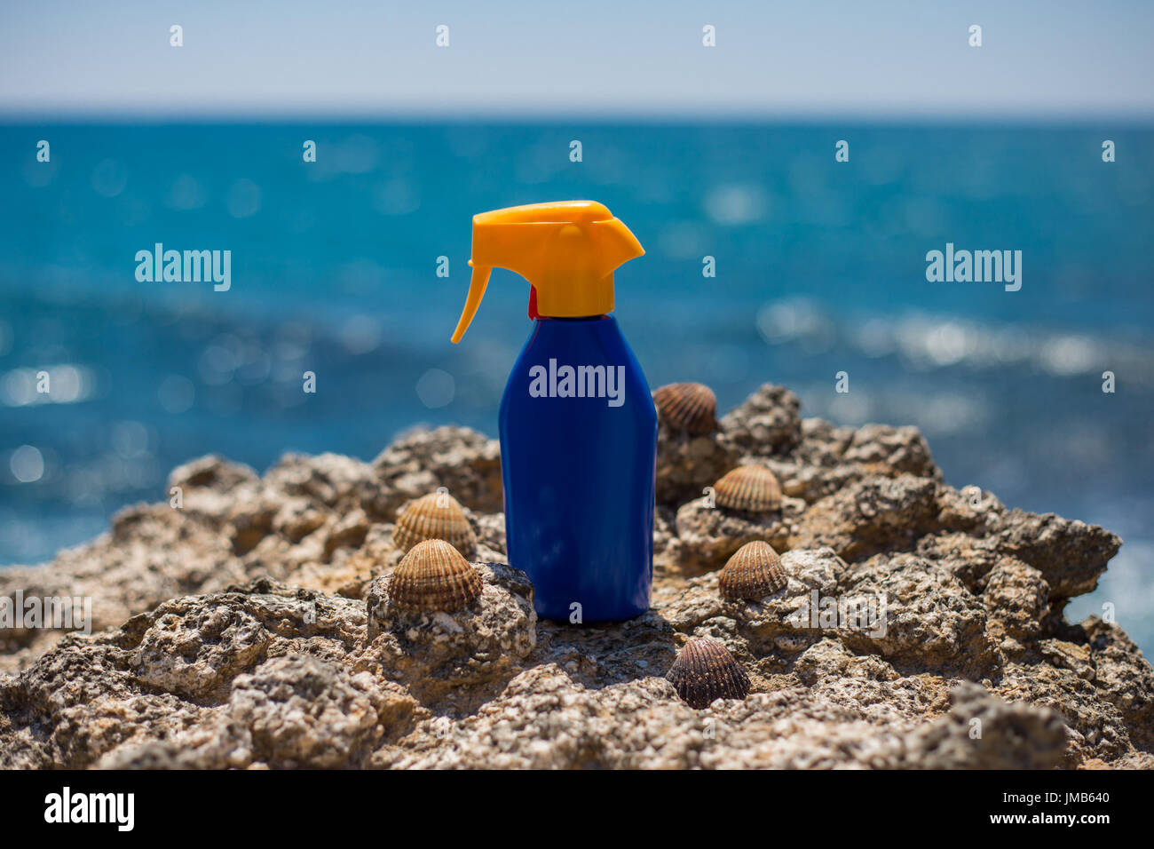 Sun cream sunscreen for tan standing on beach rocks on a sunny day with blue sea and sky in the background during summer for tanning and sunbathing ag Stock Photo